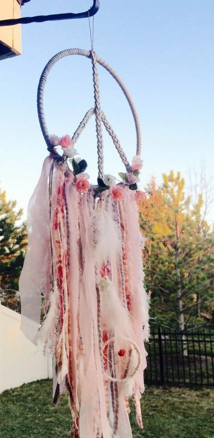 assortment of fabric strips, and ribbons in different shades of pink, tied to a large dream catcher, shaped like a peace sign
