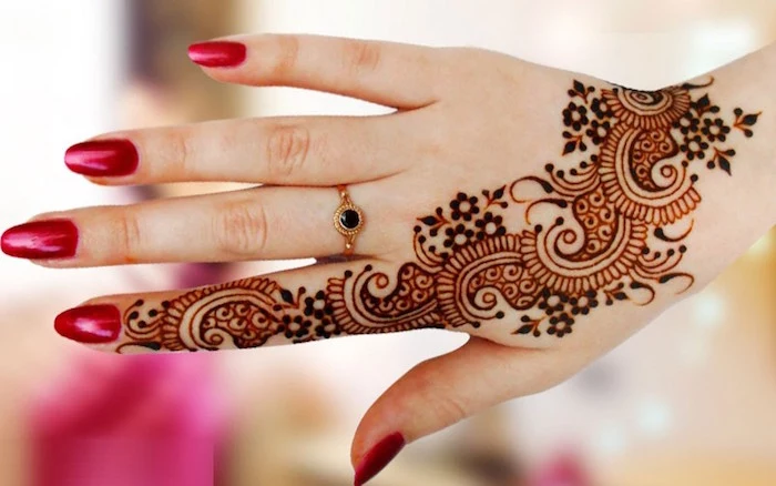 finger henna in dark brown, with flourishes and flowers, running from the tip of the index finger, to the hand's wrist