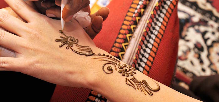 drawing floral details, on a small henna tattoo, on a person's wrist and hand, using a white cone