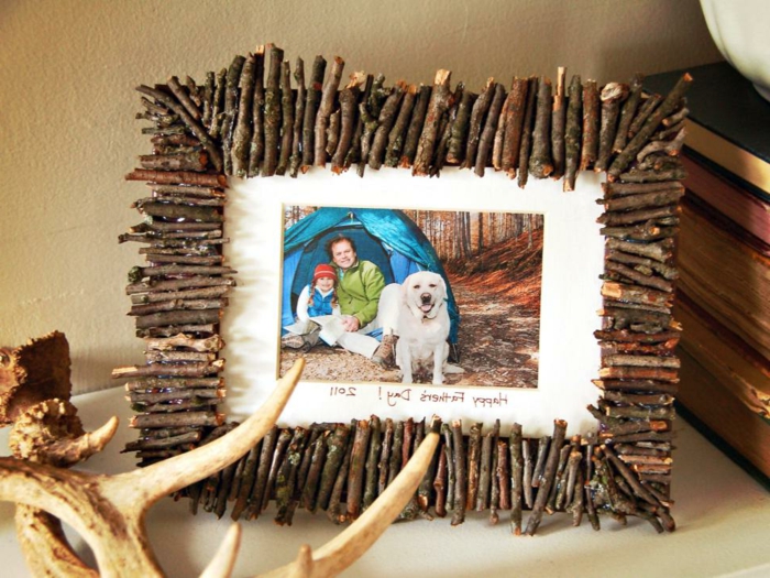 frame made from small twigs, containing a photo, of a father, his daughter and their dog, in front of a tent