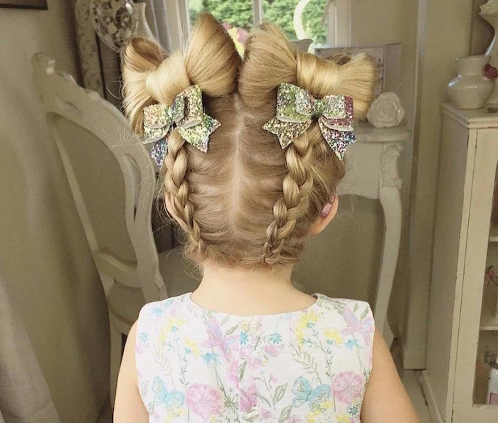 sparkly multicolored bow-shaped hair ornaments, decorating the blonde hair, of a small girl, two symmetrical braids, with bow-motifs