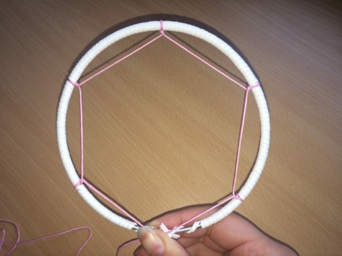 hexagonal shape made from pink string, tied to a white hoop, how to weave a dreamcatcher, held by a hand with ling nails