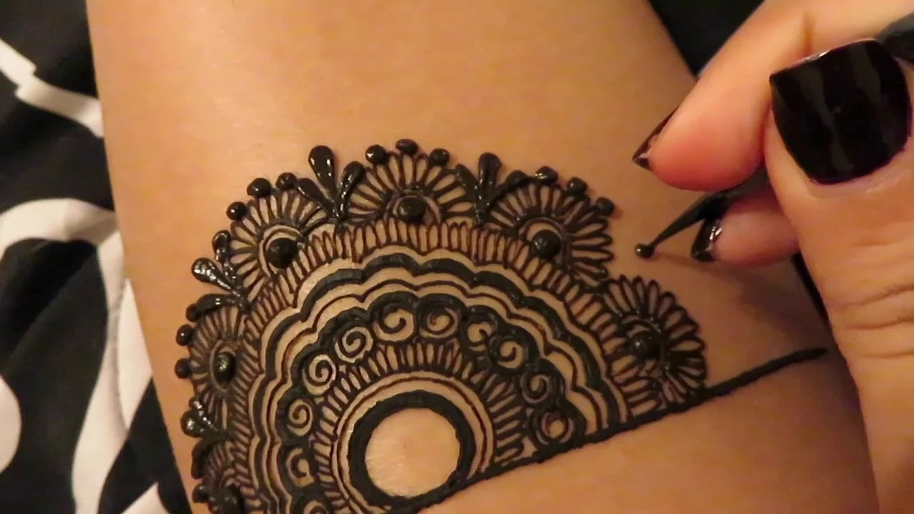 freshly made dark henna temporary tattoo, with circles and flourishes, henna meaning, hand adding a black dot, using a cone