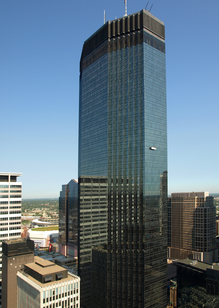 skyscraper with an unusual angular shape, made from reflective glass, and situated among smaller buildings, postmodern design