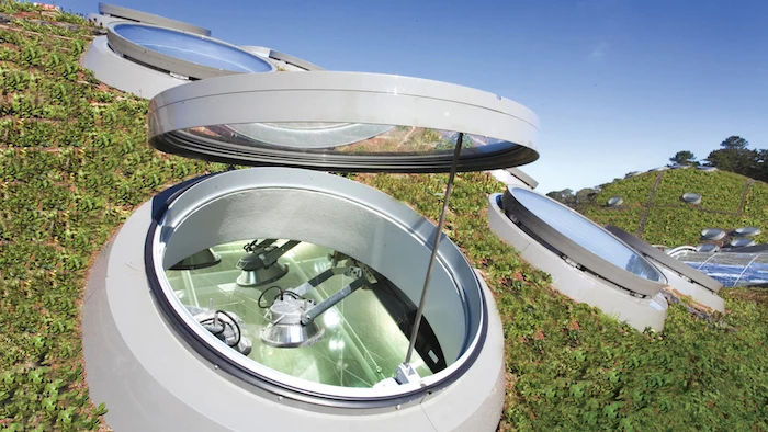 open hatch in pale grey, with a glass lid, on the roof of the california academy of sciences, surrounded by plants, postmodern buildings