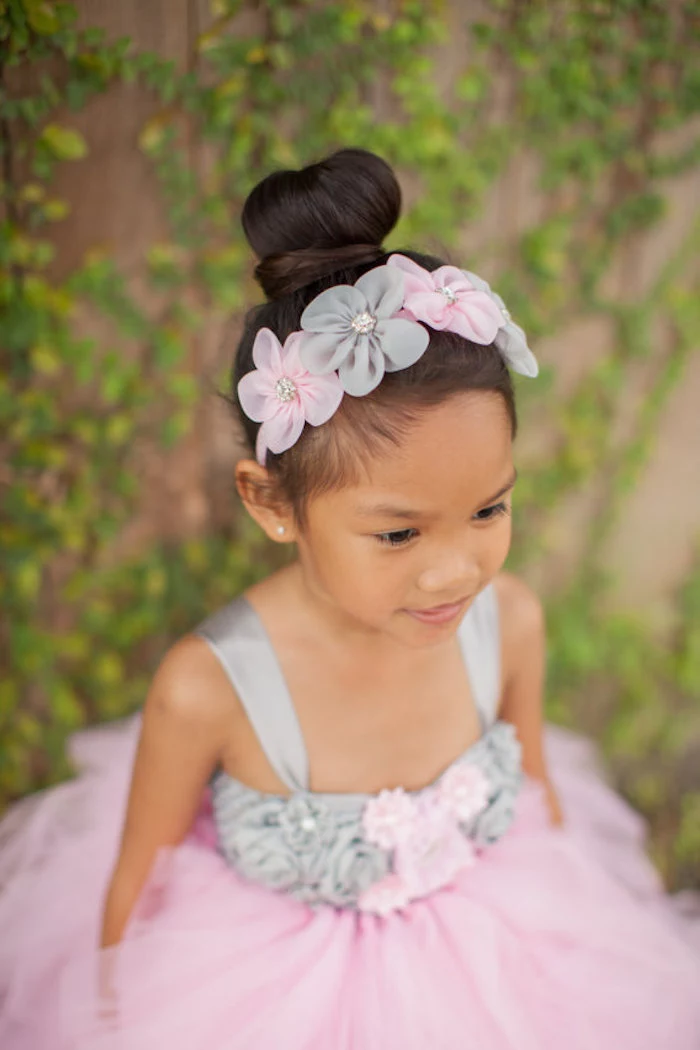topknot worn by a small girl, in a formal pale grey, and powder pink dress, little girl hairstyles, matching floral headband