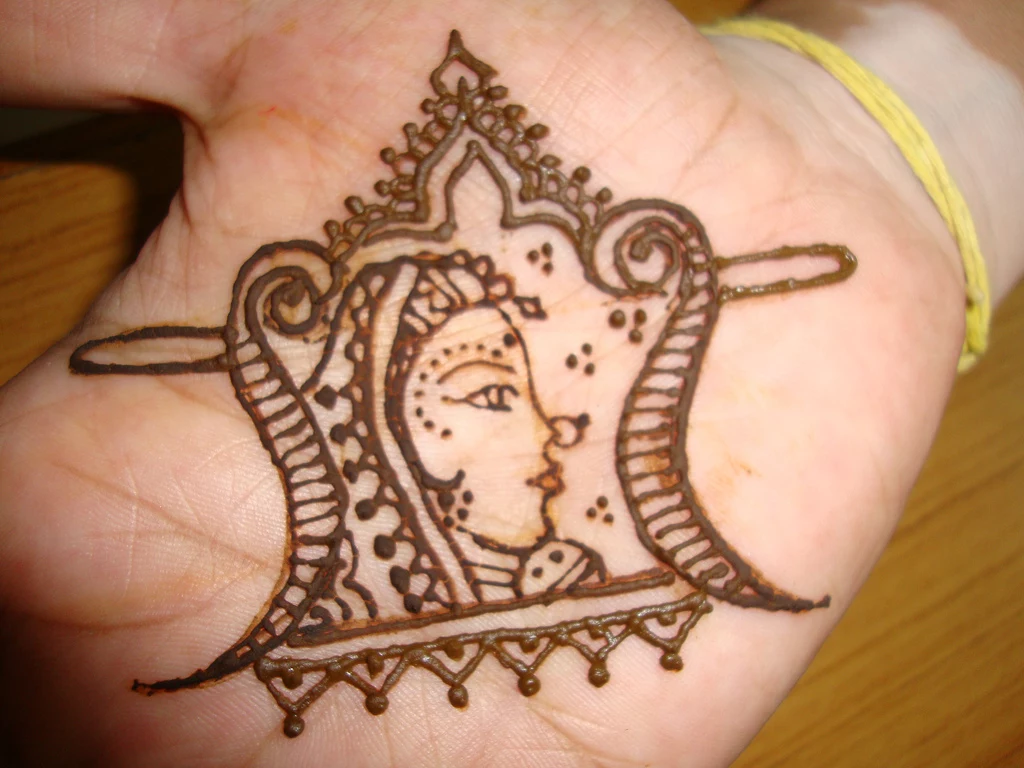 cartoon-like drawing of an indian woman, with headdress and a nose ring, done with henna, on the palm of a hand