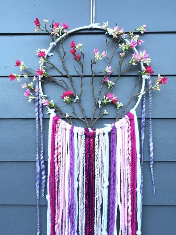 branches with faux pink, and white blossoms, decorating a dreamcatcher, with purple and maroon, white and pink tassels, big dream catchers, hung near a blue surface