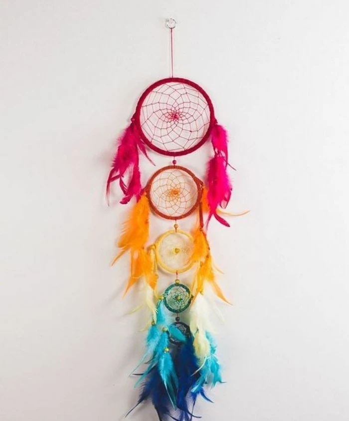 red and orange, yellow and turquoise, and dark blue, dream catcher nets, decorated with feathers in corresponding colors, and attached to one another, big dream catchers, on an off-white wall