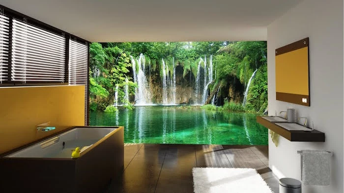 photo wallpaper with a greenish blue lake, and several waterfalls, decorating one of the walls of a room, with a white and brown bathtub, and matching brown sinks, modern bathroom ideas, brown tiled floor, and a yellow accent wall
