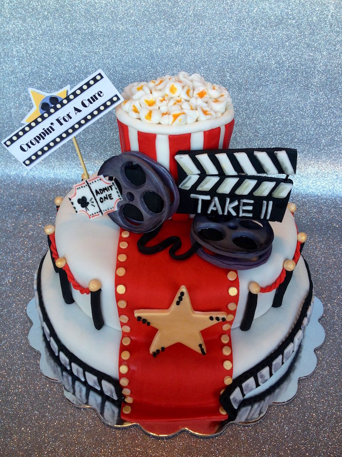 picture house-themed party cake, white with a red carpet detail, gold buttons and a large gold star, 60th birthday decorations, clapboard and popcorn, ticket and film reels