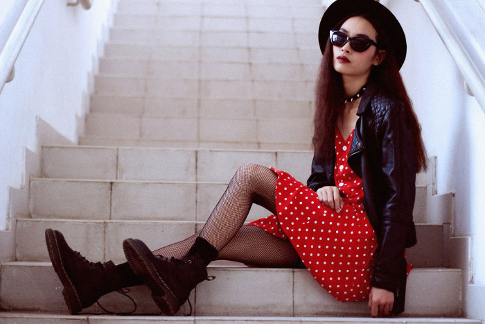 fishnet tights and black combat boots, worn with a red mini dress, with white polka dots, and a black leather jacket, by woman with sunglasses and a hat