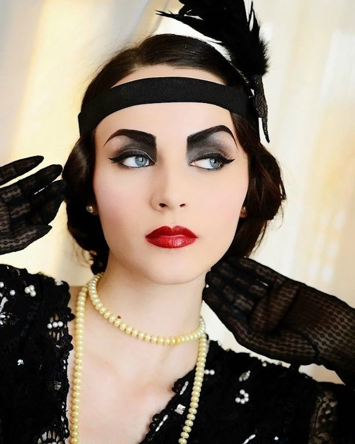 feather in black, decorating the black headband, of a woman with 1920s flapper make up, painted eyebrows and smoky eyes, bright red lipstick