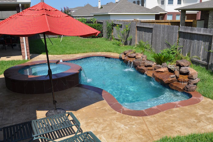 umbrella in red, near two metal sun beds, in a garden, containing a pool, decorated with stones