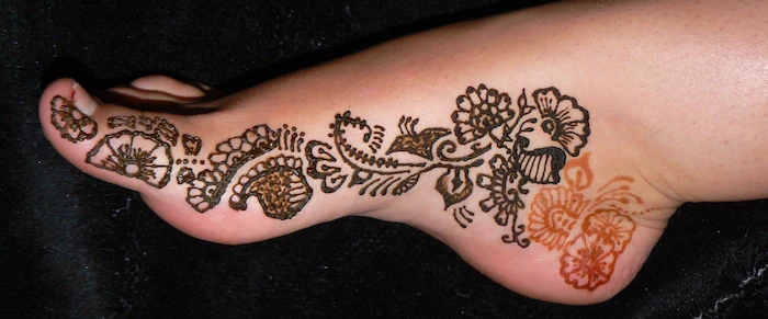 orange and dark brown areas, on a henna foot tattoo, seen in a close up, removing the top henna layer