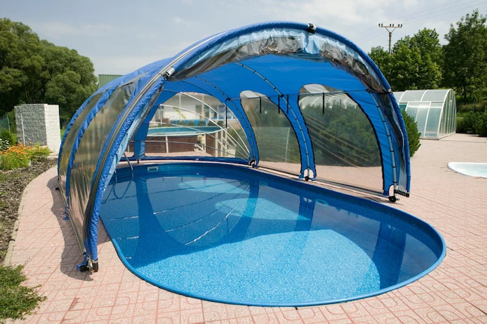 cover for a pool, made from clear, blue and black plastic, over a blue oval pool, small inground swimming pools, surrounded by beige tiles
