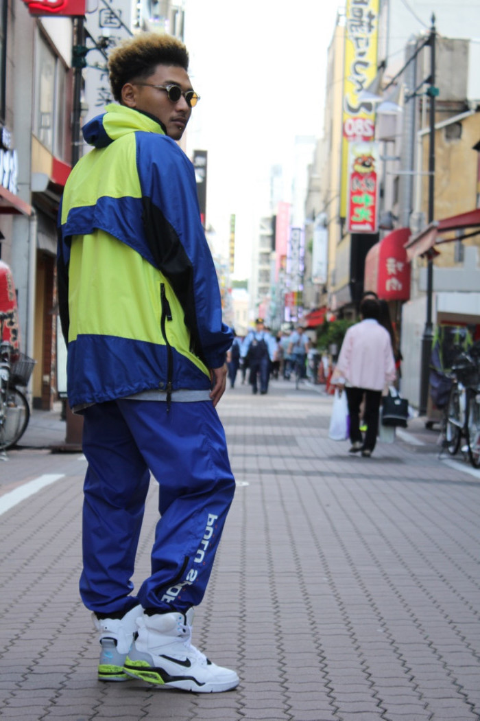 track suit in vintage style, blue and yellow, with black details and a hood, 90s halloween costumes, worn by a man with white, nike high tops, standing on a city street