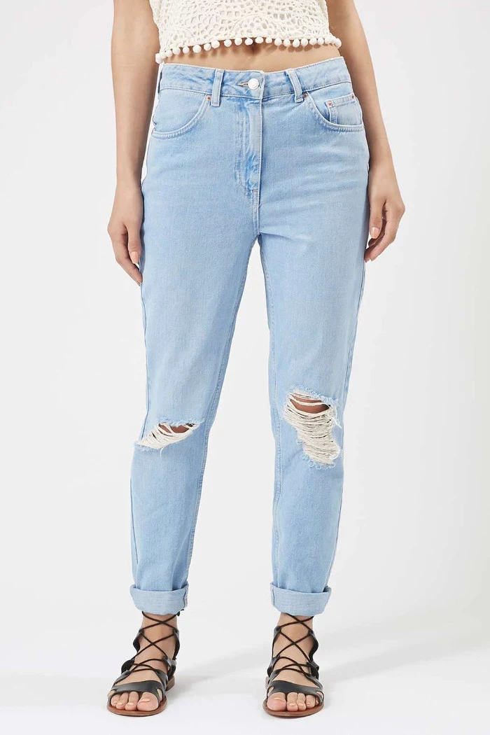 rolled-up pale blue jeans, with rips near the knees, 90s themed outfits, worn with lace up gladiator sandals, and a cropped lacy cream top