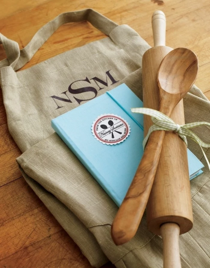 light blue recipe book, under a wooden rolling pin, and a wooden spoon, tied together with a ribbon, creative gift ideas, large burlap bag