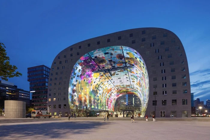 light projections in different colors, inside the hollow area of a building, with rounded edges, and many square windows, post modernity, a square with people
