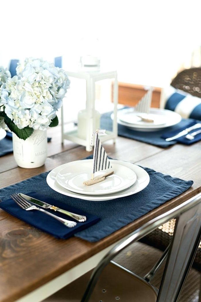 nautical table set up, in navy blue and white, 60th birthday party ideas for men, two white plates, containing a small place holder, shaped like sailing boat