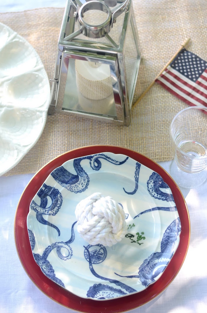 lantern made of glass, and containing candle, and a small american flag, near near a white sailor's knot, placed on a blue nautical plate, on top of a red dish, 60th birthday ideas, sea inspired setup