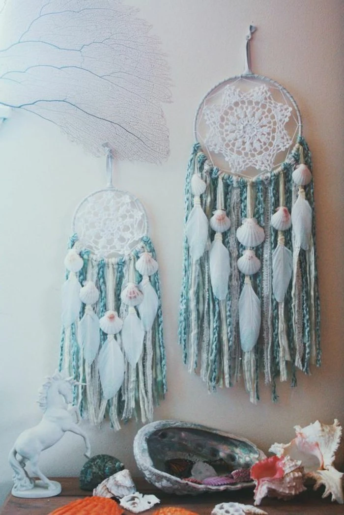 unicorn figurine in white, near two dream catchers, with white crochet doilies, teal blue tassels, white feathers and seashells
