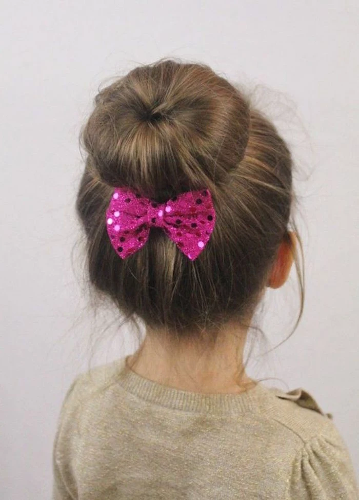 donut bun with a sparkly, sequined fuchsia pink bow, on the brunette head of a child, simple hairstyles 