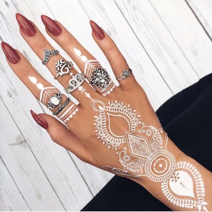 assortment of silver rings, in boho style, on a hand with long sharp red nails, decorated with cute henna, temporary tattoos in white