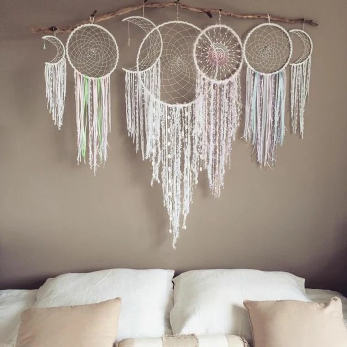 wall decoration with seven dreamcatchers, four round and three crescent shaped, hanging from a large dried branch, big dream catchers, above a bed