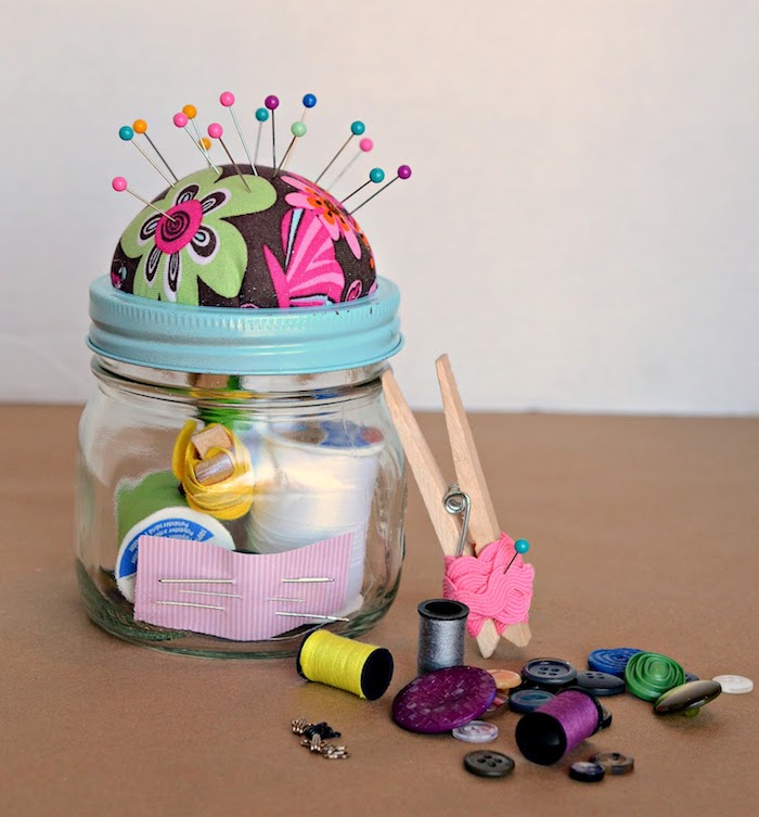 sewing station inside a glass jar with blue lid, diy christmas gifts for boyfriend, buttons yarn and needles, on a brown surface