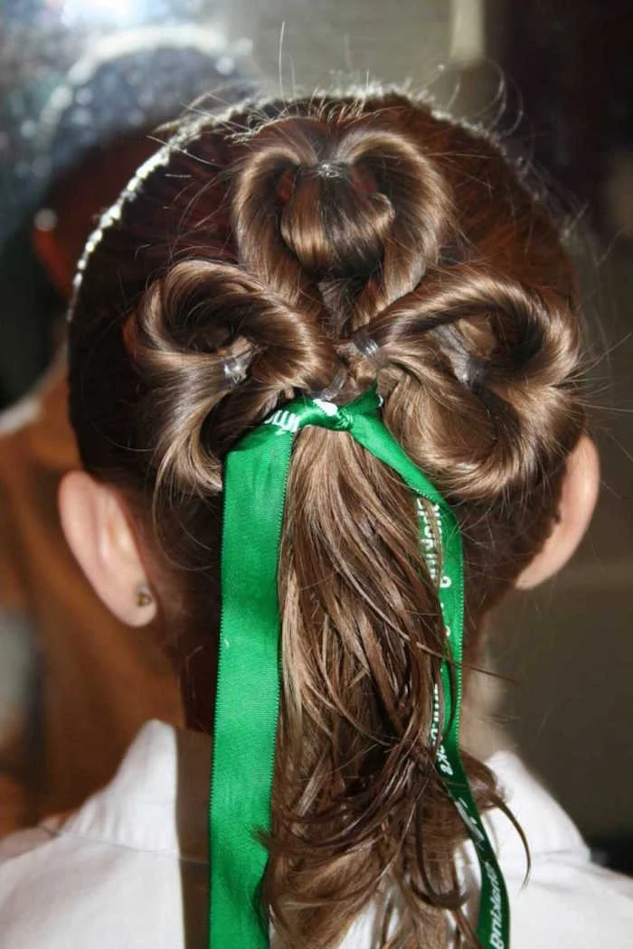 clover-like hair braid, decorated with a green ribbon, on the brunette head of a young girl, st. patrick's day little girl haircuts, shamrock motif