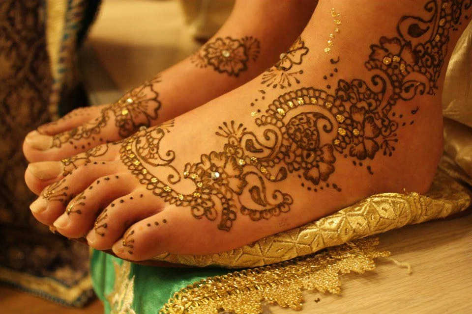 tiny shimmering gold details, decorating a henna foot tattoo, identical flower design, on two bare feet