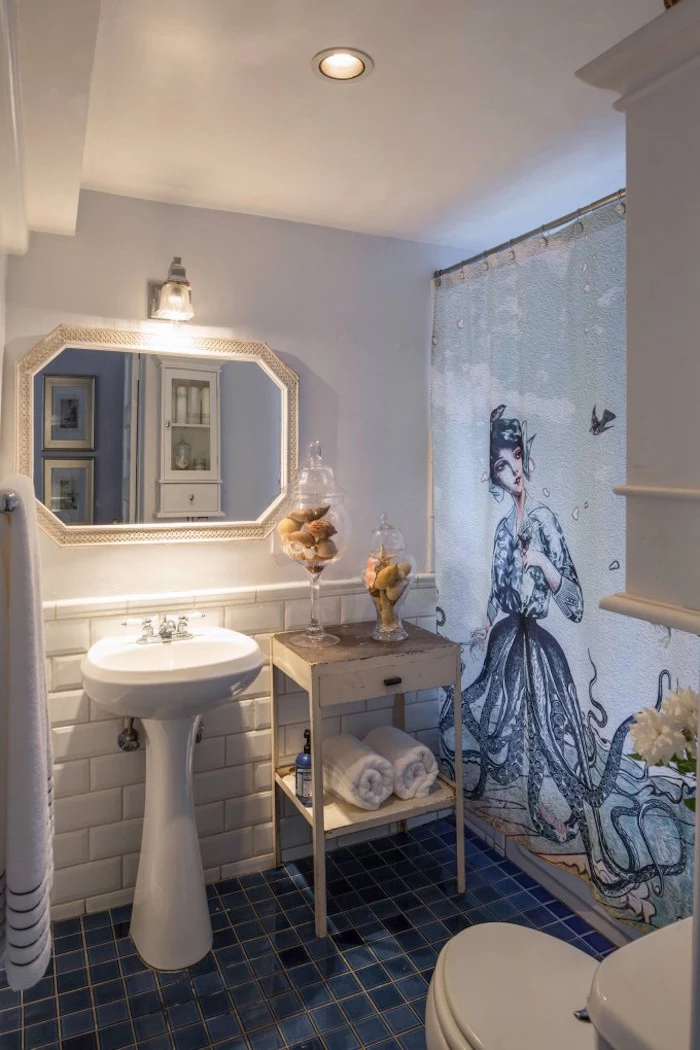 graphic print, of an octopus mermaid, on a shower curtain, in a bathroom with pale walls, decorated with white subway tiles, small bathroom decoration ideas, shabby chic cabinets, and two glass containers, filled with seashells
