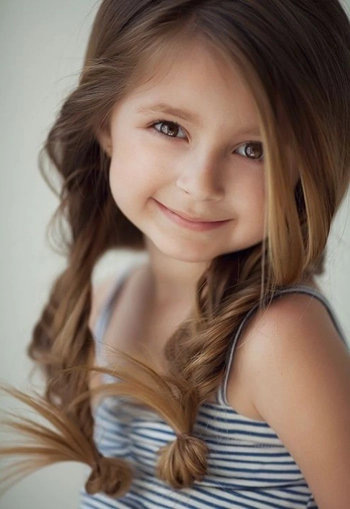 herringbone braids on smooth, long brunette hair with side part, worn by a smiling little girl, simple hairstyles, striped white and navy top