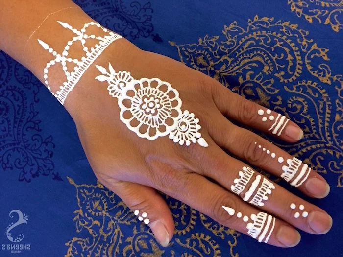 easy design in white, small henna tattoo, with stripes and flowers, on a person's fingertips, hand and wrist