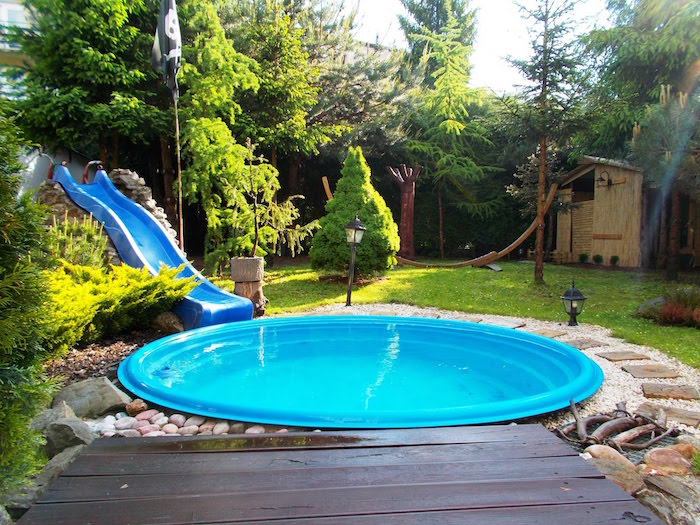 tool shed and various trees, in a garden, containing a small, round shallow pool, and a plastic slide, cool backyards, lawn with green grass and pebbles