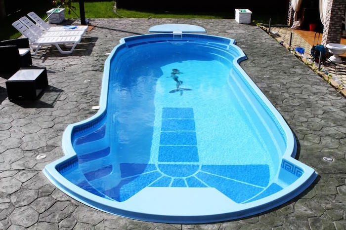 mermaid decal on the bottom of a blue pool, filled with water, and surrounded by grey stone tiles, small inground swimming pools, three white sun beds nearby