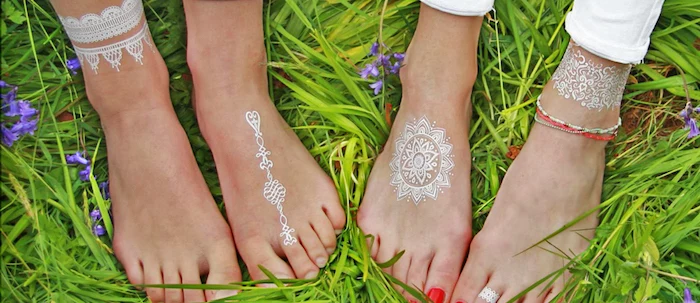 grass in a fresh green color, under two sets of feet, each decorated with a white, small henna tattoo