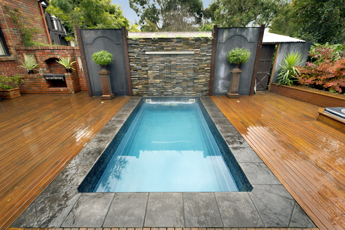 symmetrical set up, with a rectangular pool, surrounded by a small column, with a green plant, on each side, backyards with pools, wet wooden planks covering the ground