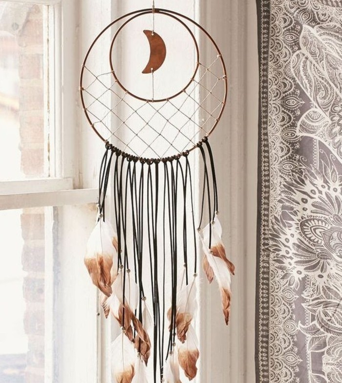 window decorated with a diy dreamcatcher, featuring a small, crescent moon ornament, and black tassels, with white feathers, dipped in brown paint