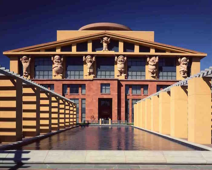 statuettes of the seven dwarves, from the animated movie snow white, propping a roof, with elements inspired by antiquity, on a yellow and orange building, disney studio's HQ in Burbank