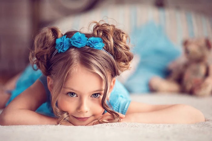 turquoise blue flower hair ornament, on the head of a smiling child, with two curly buns, on the sides of hr head, hairstyles for little girls