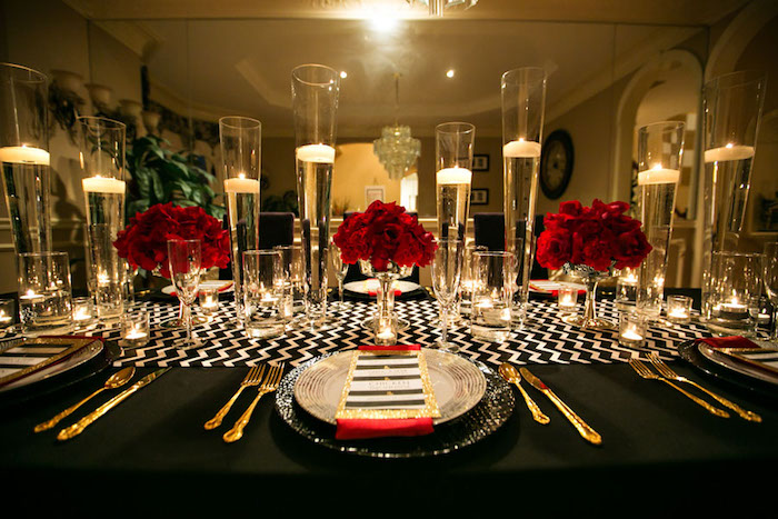 table cloth in black, with white zig-zag details, on a table set for a fancy dinner, gold cutlery and candles in tall glasses