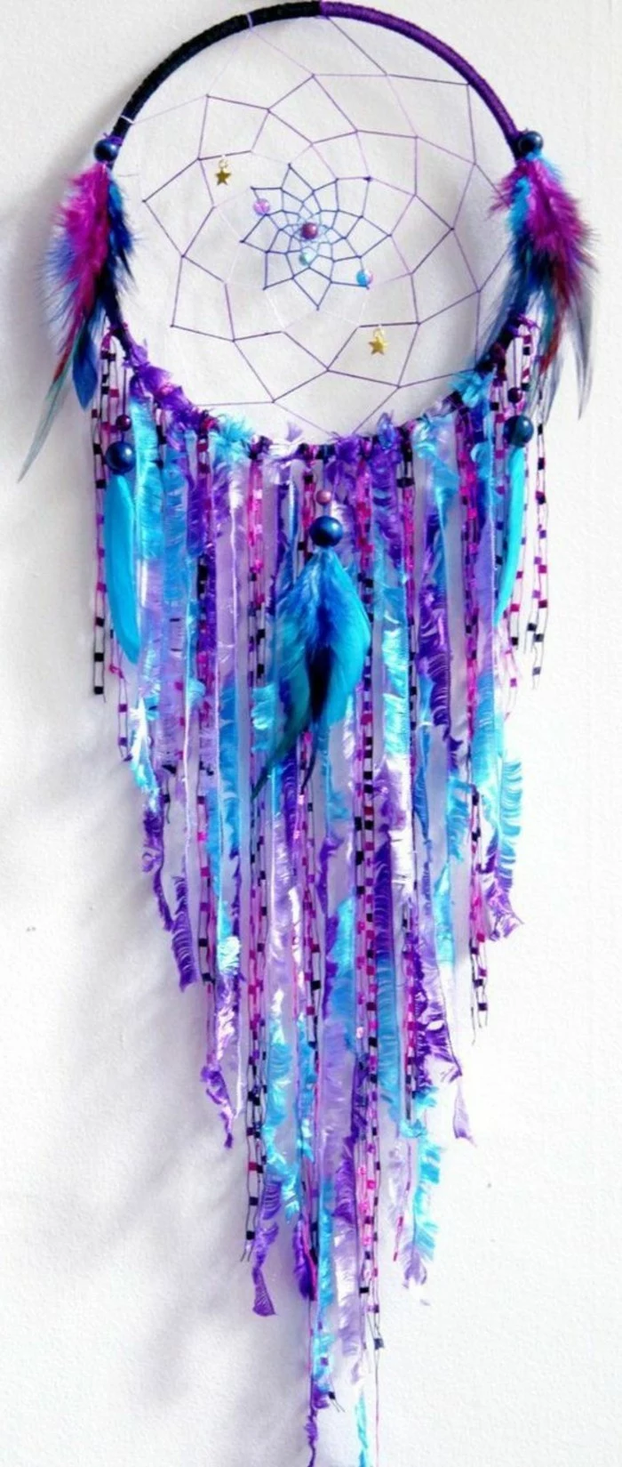 big dream catchers, purple and turquoise, beads and feathers, and strips of ribbon, decorating a dream catcher, mounted on a white wall