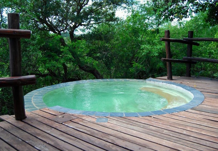 circular pool on a terrace, covered in wooden planks, and featuring a wooden fence, pool patio ideas, with a forest view