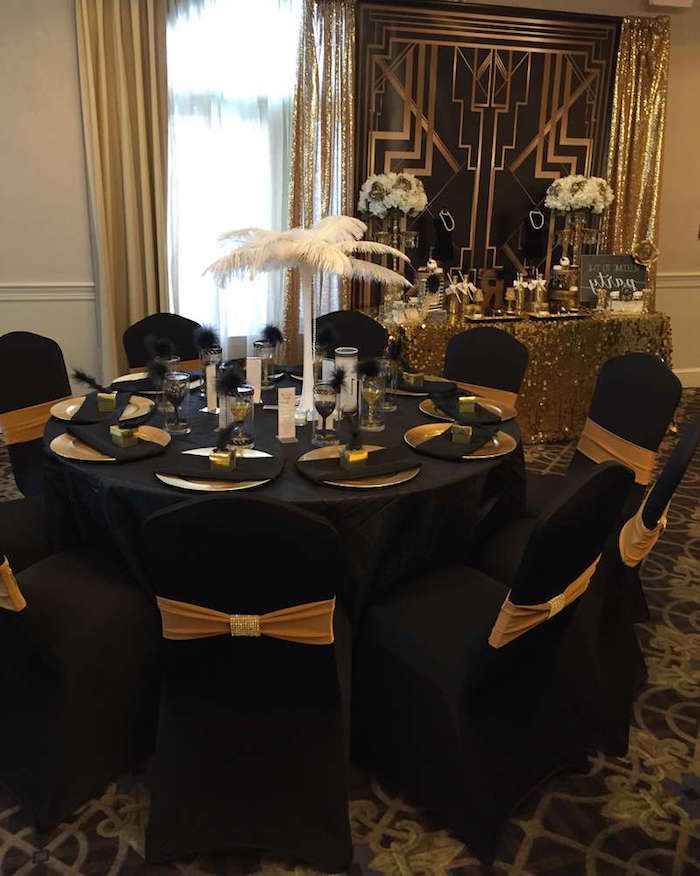 60th birthday color, round black table, with black chairs, decorated with a white ostrich feather center piece, and gold details, art deco motifs, jazz age birthday party