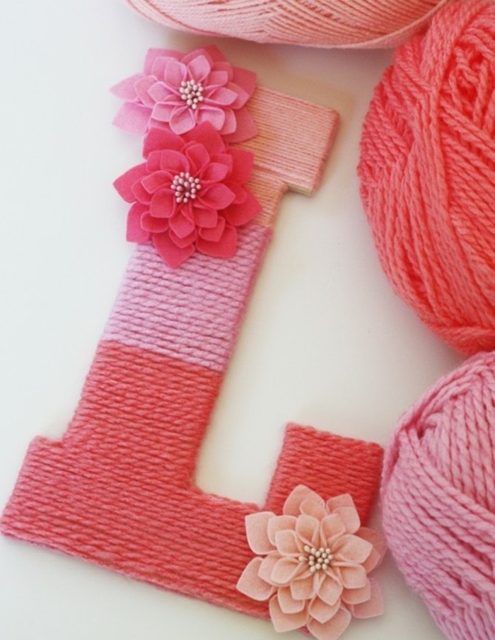 yarn in three different shades of pink, wrapped around a big L shape, decorated with pink flower ornaments, cute gift ideas, three balls of yarn nearby
