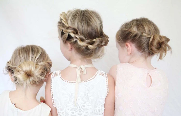 embroidered pale cream, and white formal dresses, worn by three small girls, with blonde hair, each styled in a different up-do, braids and buns, little girl hairstyles