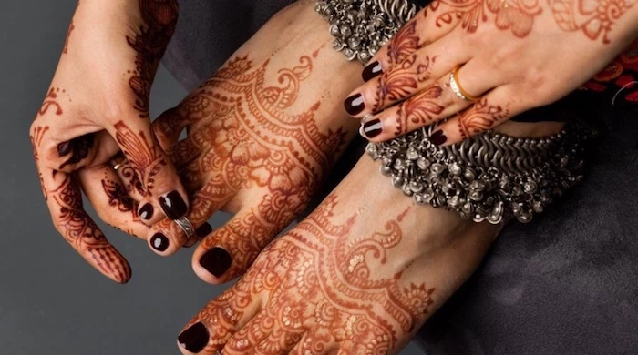 cherry red nail polish, on the fingernails and toes of a woman, putting a ring on one of her toes, temporary henna tattoos, on her feet and hands